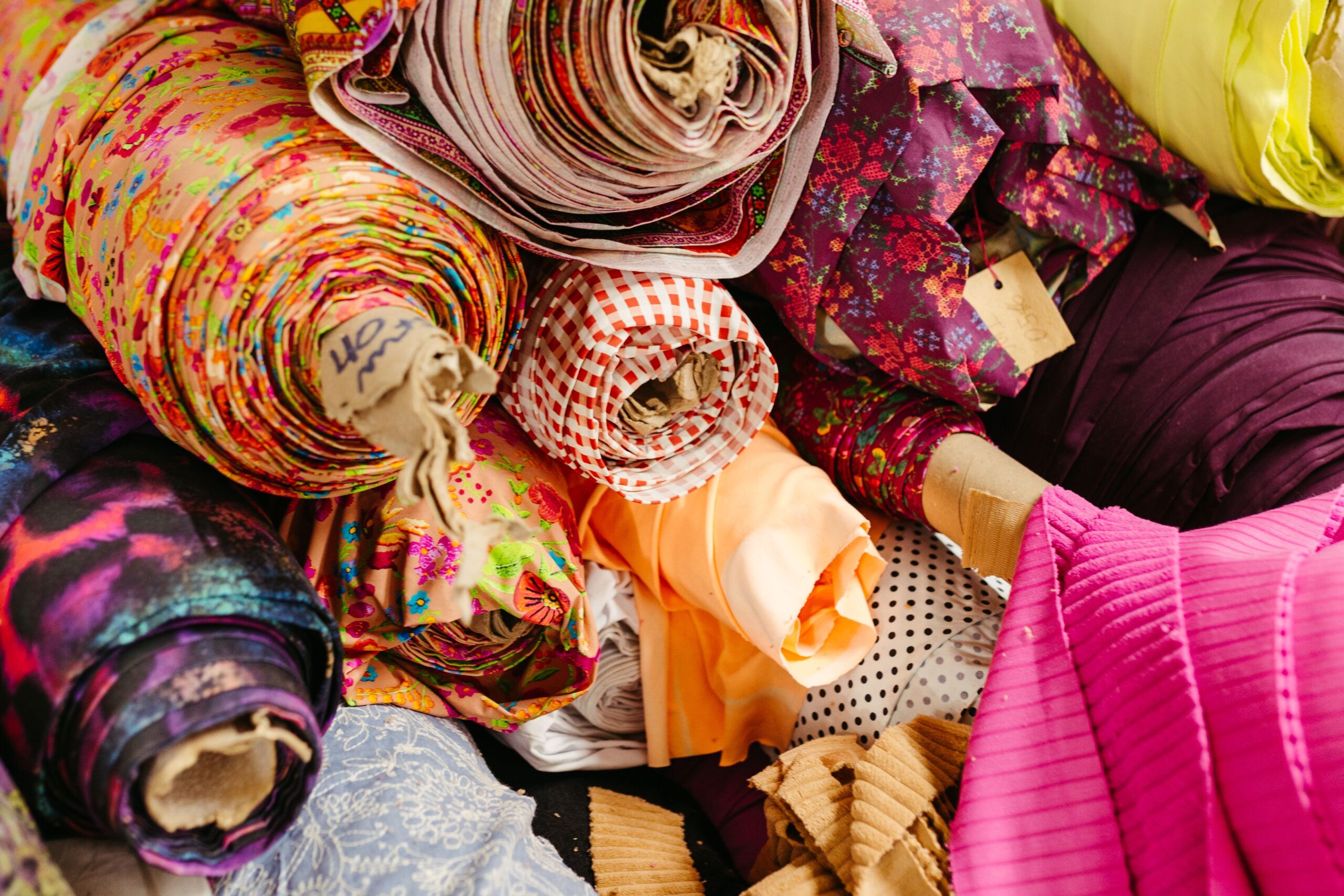 A vibrant collection of multicolored fabric rolls and swatches, arranged in a neat pile